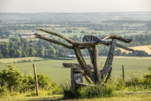 A wooden sculpture sits high on a hilltop with a view of fields and trees below it