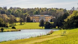 The yellow and white palladian mansion West Wycombe House, showing the lake and woodlands in the background.